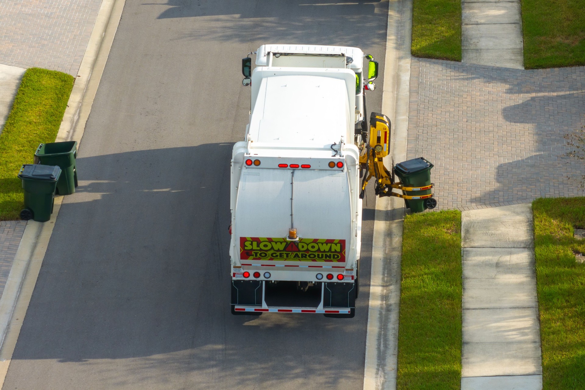 Weekly clean-up. Garbage truck picking up trash bins from the curb in American suburban neighborhood
